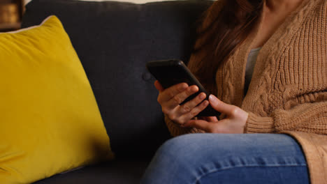 Close-Up-On-Hand-Of-Woman-Sitting-On-Sofa-At-Home-Using-Mobile-Phone-To-Check-Social-Media-Message-And-Scrolling-Online-3